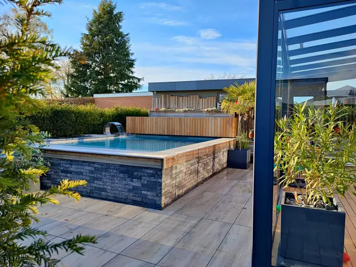 Piscine semi-enterrée habillée de parement pierre, terrasse en dalles imitation bois