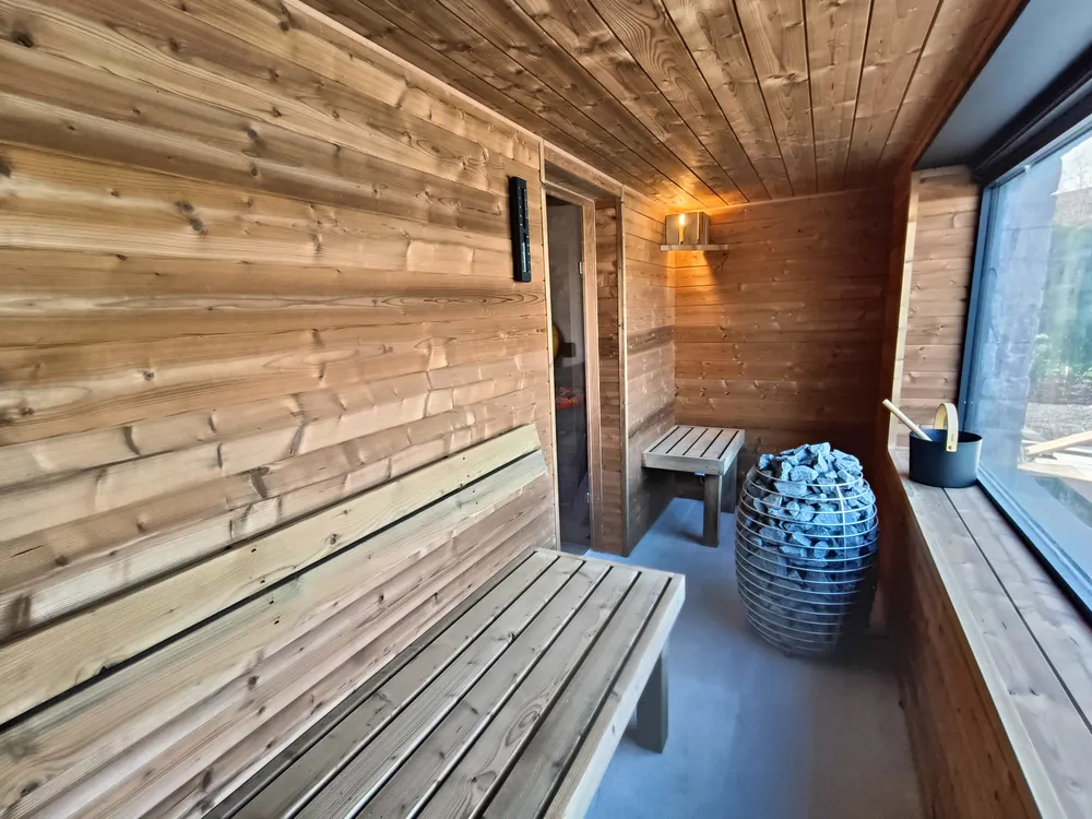 Sauna en thermobois posé par Sebonard en province de Liège : banquettes, poêle à pierres et baie vitrée